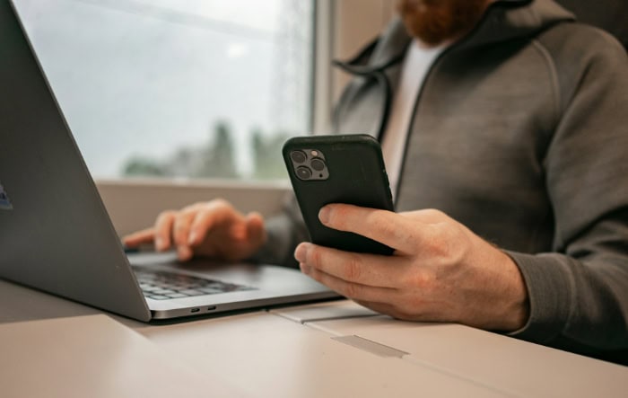 Man using smartphone and laptop near window in office