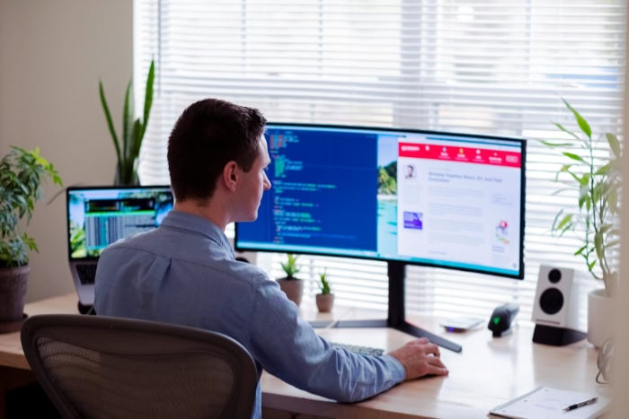 Man working at desk with dual monitors and laptop