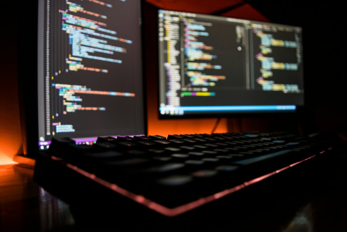 Mechanical keyboard glowing with code on dual monitors