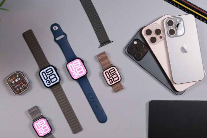 Multiple Apple Watches and iPhones on grey desk