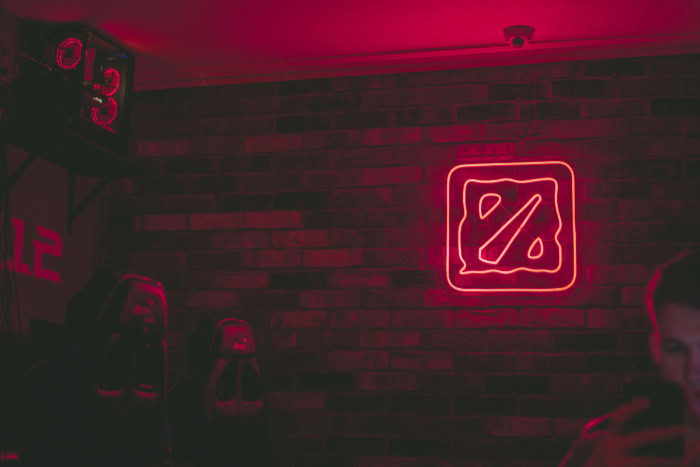 Neon Dota 2 logo on brick wall in gaming venue