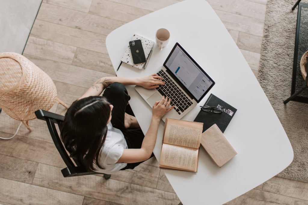 Overhead view of woman using laptop with books on desk