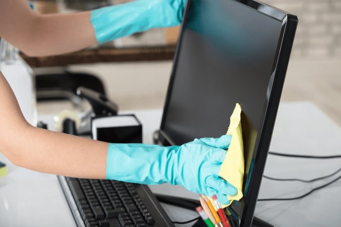 Person cleaning computer screen with yellow cloth