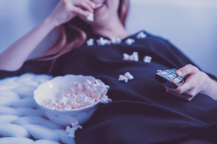 Person eating popcorn while holding a TV remote