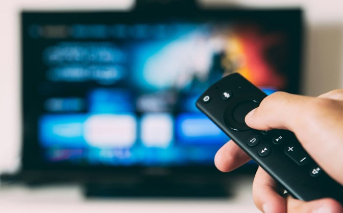 Person holding TV remote control in front of screen