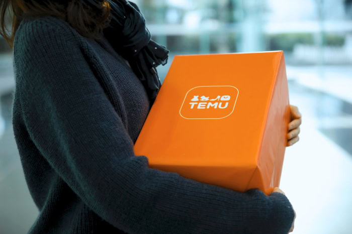 Person holding a bright orange Temu delivery