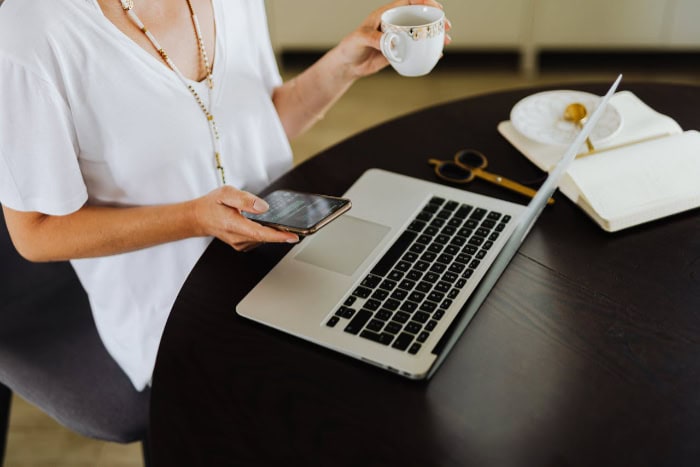 Person holding a phone and coffee near a laptop