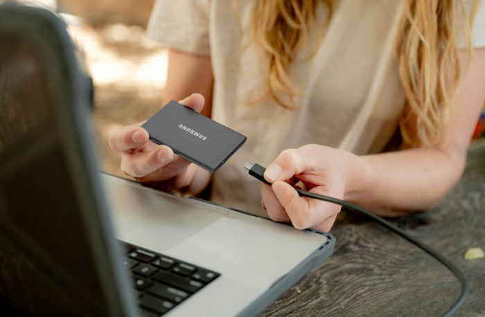 Person holding a portable Samsung SSD connected to a laptop