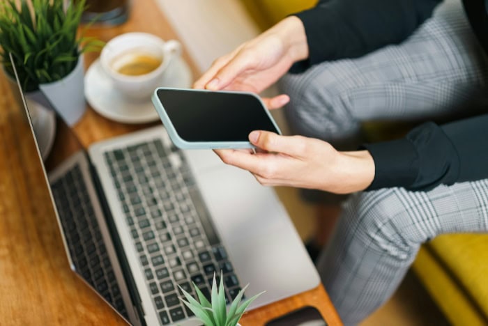 Person holding a smartphone near a laptop