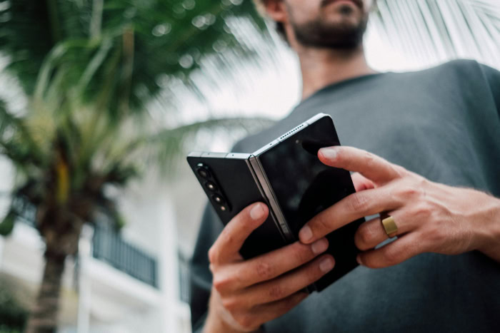 Person holding foldable phone outdoors near palm trees