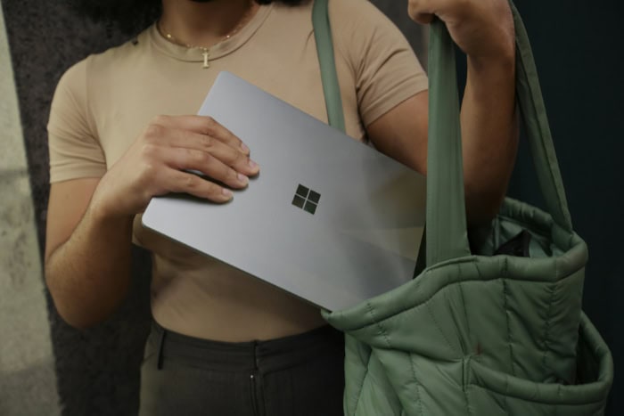 Person holding silver Microsoft Surface laptop with green bag