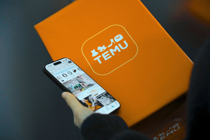 Person holding smartphone next to orange Temu