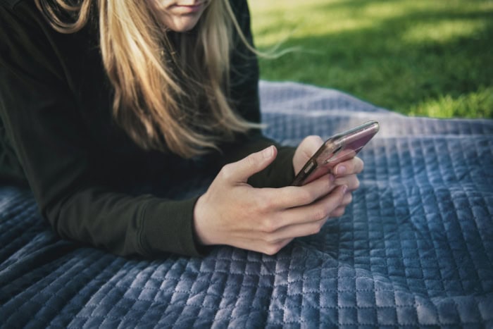 Person lying on blanket using a smartphone outdoors