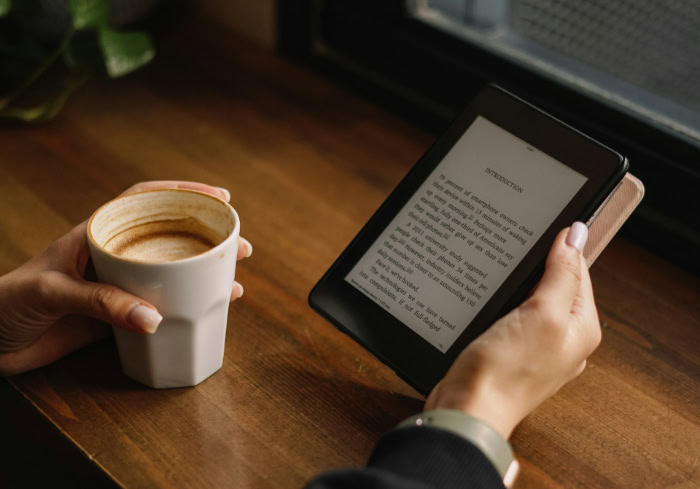 Person reading Amazon Kindle e reader with coffee cup