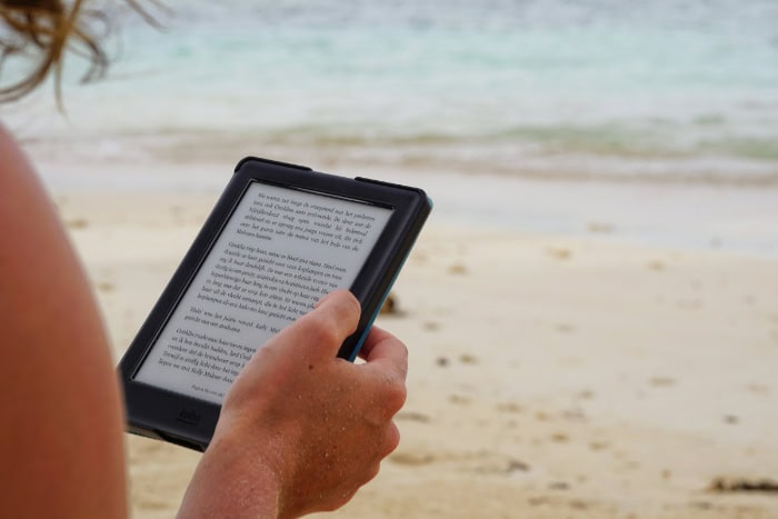 Person reading a Kindle on a sandy beach