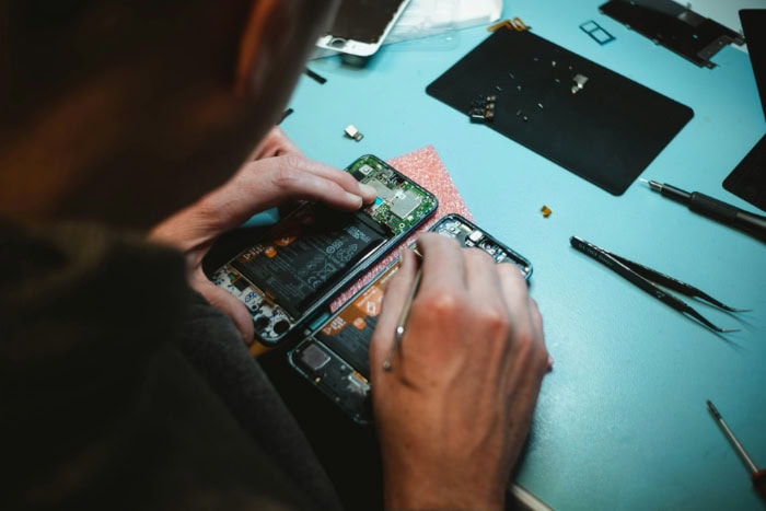 Person repairing disassembled smartphone with tools on blue surface