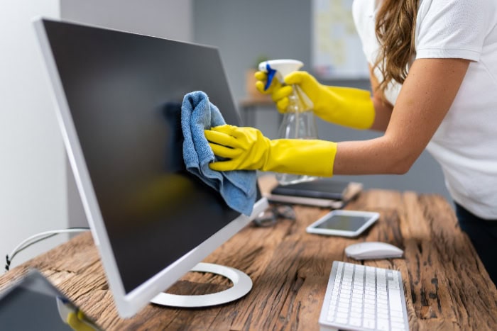 Person spraying and wiping computer screen with blue cloth