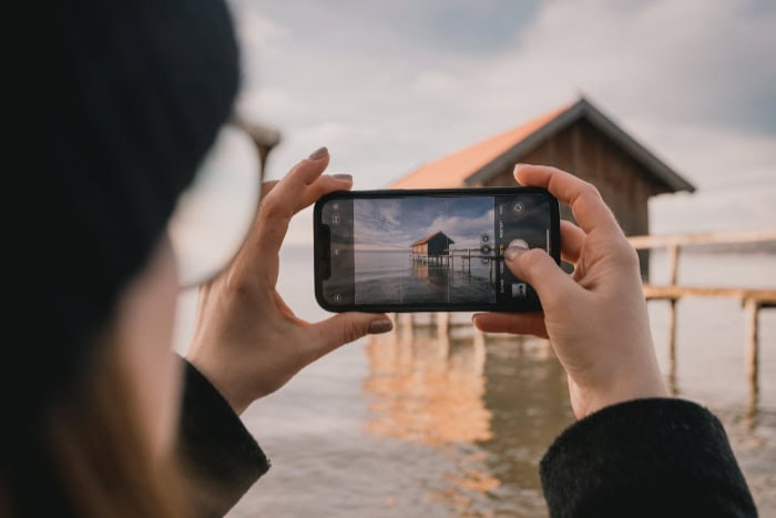 Person taking a photo of a lakeside house with a smartphone