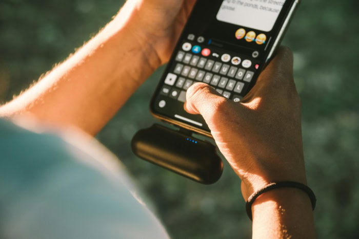 Person texting on a smartphone with a small power bank attached