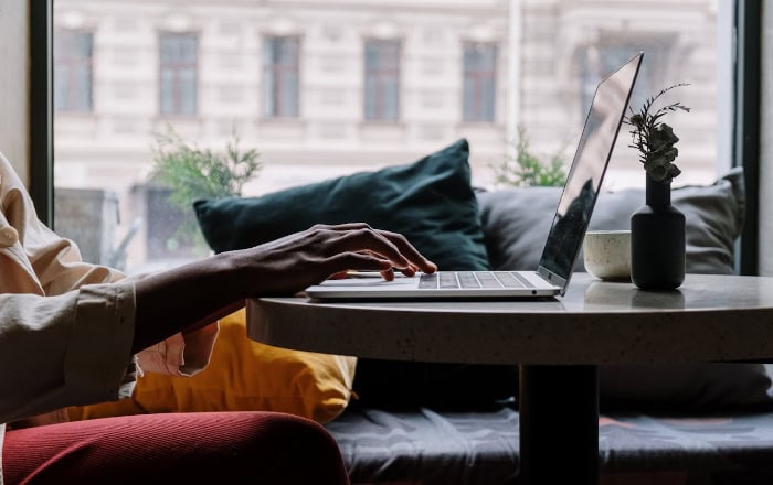 Person typing on laptop at table with plants and window view