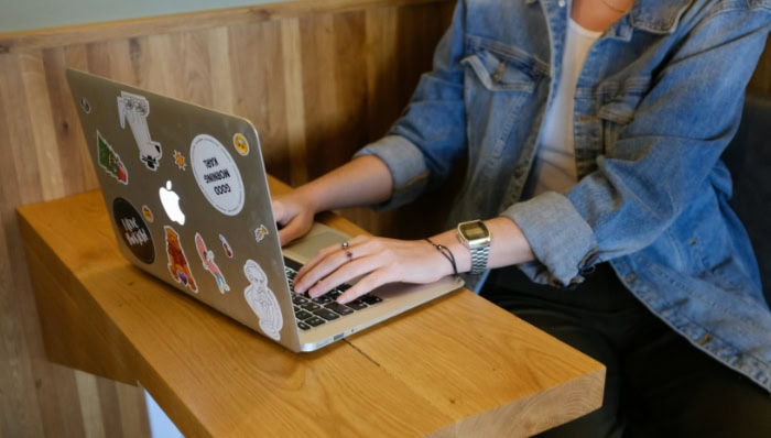 Person typing on laptop covered with stickers on wooden desk