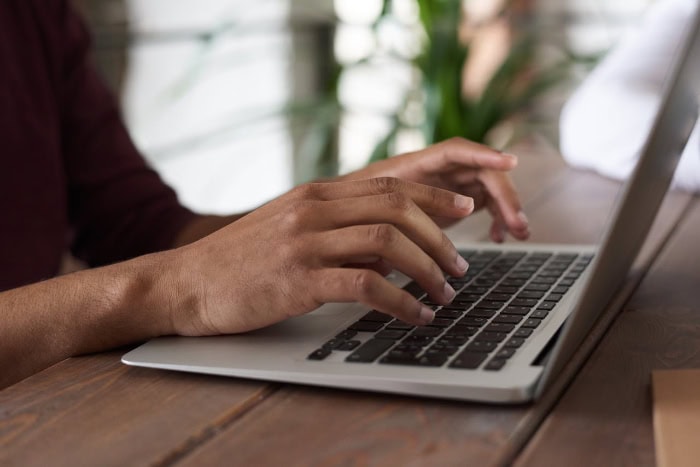 Person typing on laptop keyboard at wooden desk