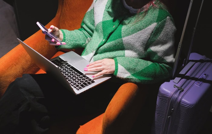 Person using laptop and smartphone while traveling with luggage