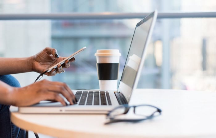 Person using laptop and smartphone with coffee cup nearby