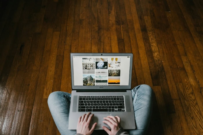 Person using laptop on wooden floor viewing photo gallery