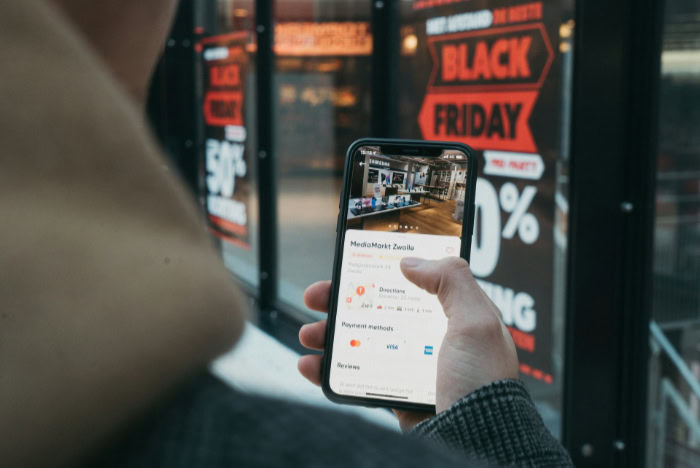 Person using smartphone near Black Friday sale advertisement