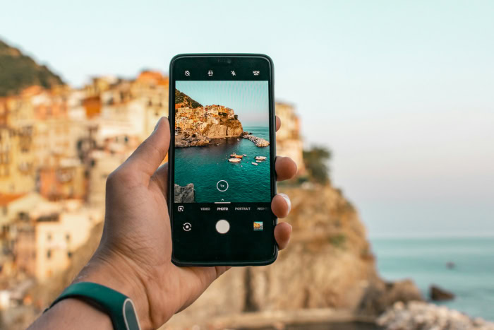 Person using smartphone to photograph scenic coastal village
