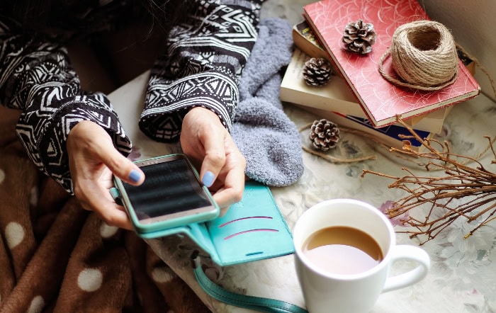 Person using smartphone with winter decor and coffee nearby