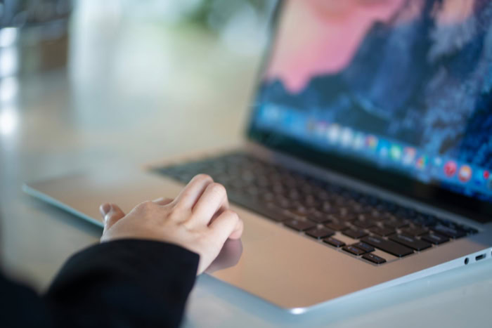 Person using trackpad on a silver MacBook laptop