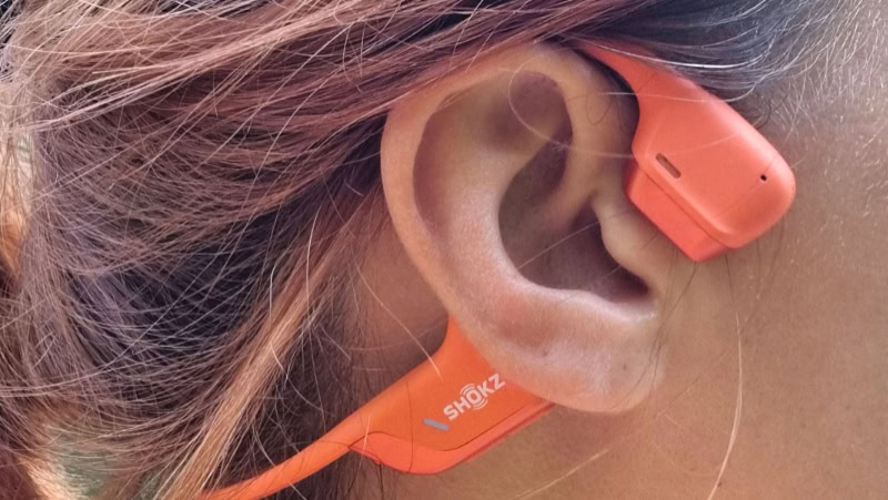 Person wearing orange Shokz bone conduction headphones