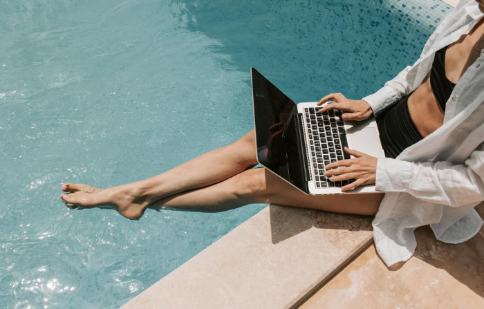 Person working on a laptop while sitting by the edge of a swimming pool