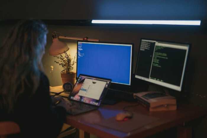 Person working on multiple computer screens in dimly lit room