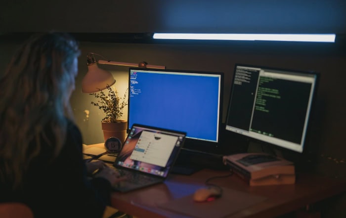 Person working on multiple computer screens with code visible