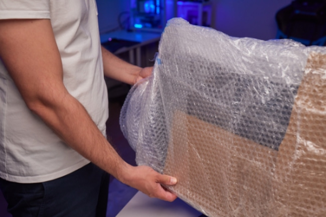 Person wrapping a flat screen monitor in bubble wrap in a home office setting