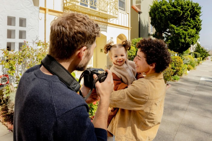 Photographer capturing a smiling child held by parent outdoors