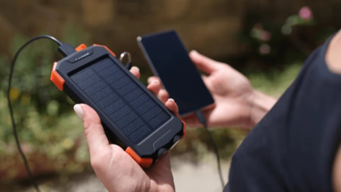 Portable solar power bank charging smartphone in hand