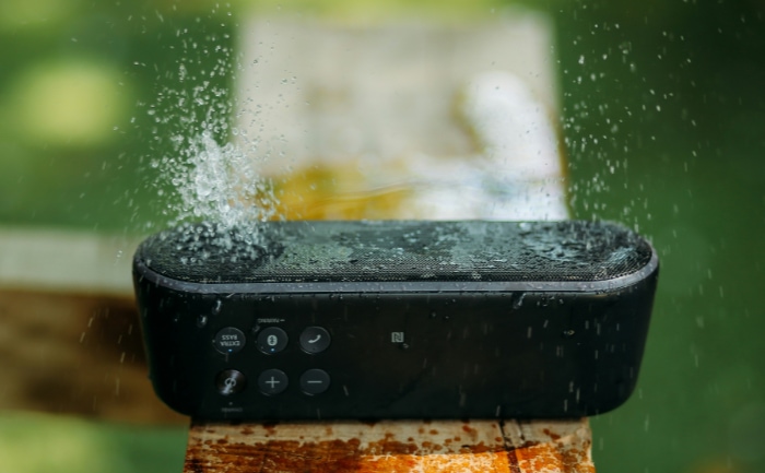 Portable speaker on a wooden surface with water splashing on it