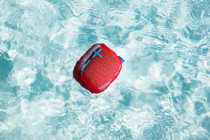 Red waterproof portable speaker floating in clear water