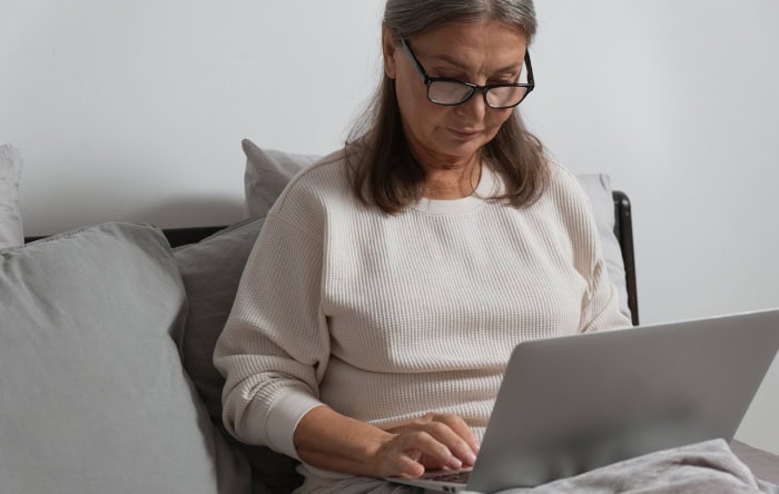 Senior woman using laptop on couch focused on screen