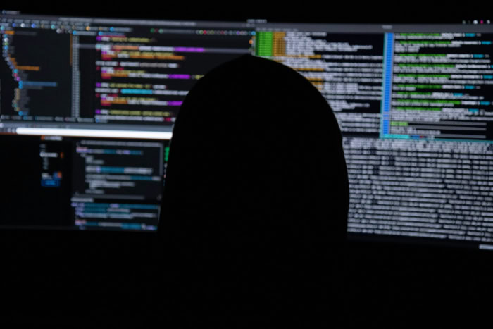 Silhouette of person viewing code on multiple monitors