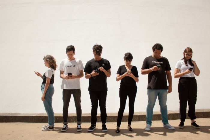 Six people using smartphones while standing in a line