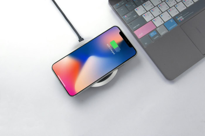 Smartphone charging wirelessly on pad next to laptop