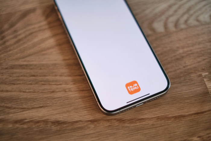 Smartphone displaying Temu app logo on wooden surface
