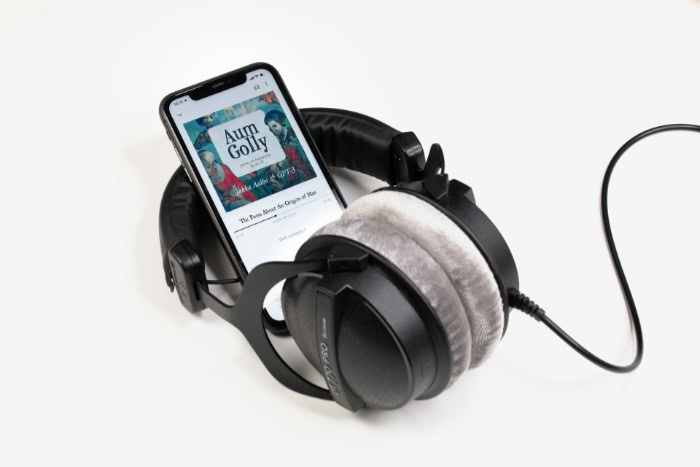 Smartphone playing audiobook resting on black over ear headphones