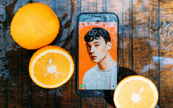 Smartphone with a water droplet covered screen resting beside sliced oranges