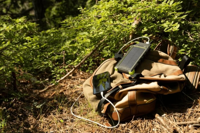 Solar power bank charging phone on backpack outdoors